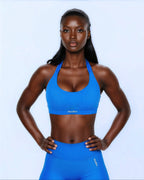Woman wearing a blue sports bra and leggings with 'Alura' branding on a light gray background
